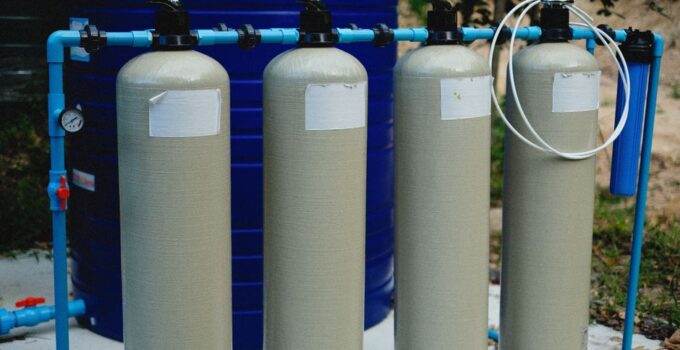 Four beige tanks in an outdoor water treatment setup with blue piping.