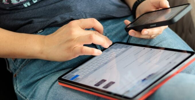 Close-up of adult using a tablet and smartphone indoors, showcasing digital connectivity and multitasking.